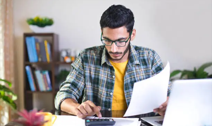 Man reviewing paperwork and using calculator.